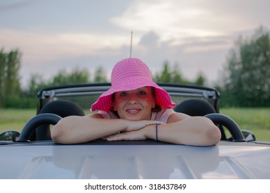 Schöne junge Frau in weißem Hemd und rosa Hut, lächelnd aus einem Auto.