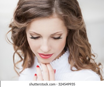 Hermosa joven romántica elegante cara de mujer, tiene los ojos cerrados, cabello natural de cabello, pestañas largas, mano con manicura roja, labios sensuales. Maquillaje puro. Blusa blanca. Tinte natural