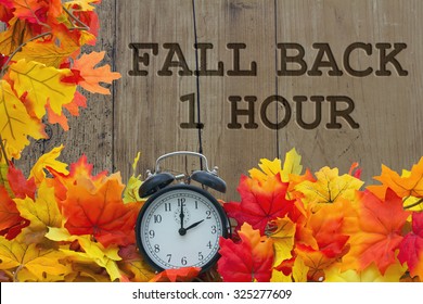 Herbstzeitumstellung, Herbstblätter und Wecker mit Grunge-Holz mit Text Fall Back 1 Hour
