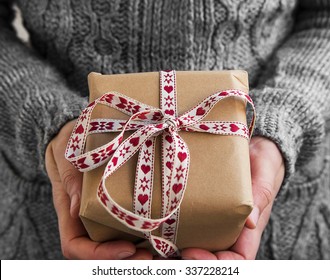 Mujer sosteniendo un regalo de Navidad decorado rústico con cinta roja y blanca