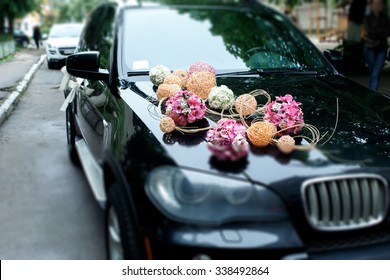 Una elegante decoración de flores blancas, cintas y bolas rosas en un coche de bodas bmw brillante