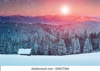 Colorido atardecer en las montañas de invierno. Bosque nevado y cabaña en el fondo de los copos de nieve que caen.
