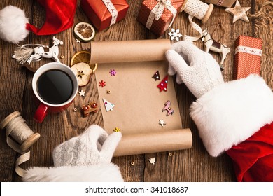 Santa Claus with gifts and wish list on wooden table