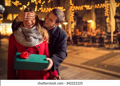 El hombre mantiene a su novia con los ojos cubiertos mientras le da un regalo, una sorpresa romántica para Navidad