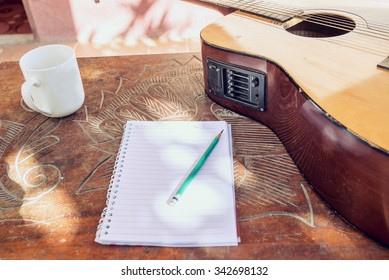 Guitarras acústicas con un cuaderno y una taza de agua en la mesa bac