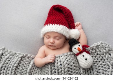 かぎ針編みのサンタ帽子と雪だるまのぬいぐるみをかぶって眠っている、生後 2 週間の新生児の男の子。