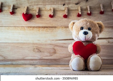 Teddybär, der ein herzförmiges Kissen mit Plankenholzbretthintergrund hält