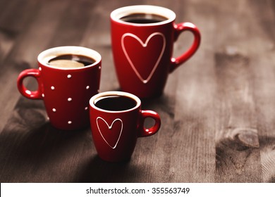 Three red coffee cups, with hearts and polka dots, standing on black wooden surface with place for text. Coffee for St. Valentine's Day.