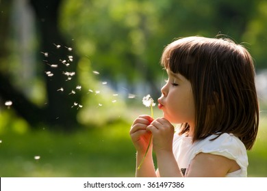 春の公園でタンポポの花を持つ美しい子。屋外で楽しんで幸せな子供。