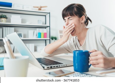 Mujer somnolienta cansada bostezando, trabajando en el escritorio de la oficina y sosteniendo una taza de café, exceso de trabajo y concepto de privación del sueño