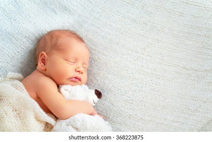 Em bé sơ sinh dễ thương ngủ với một con gấu bông đồ chơi màu trắng