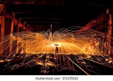 Burning steel wool spinned in urban area. Showers of glowing sparks from spinning steel wool. Man in the fire. (Night photo without effects with little noise)