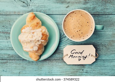 Kaffeetasse mit Croissant und Notizen Guten Morgen auf türkisfarbenem rustikalem Tisch von oben, gemütliches und leckeres Frühstück, vintage getönt