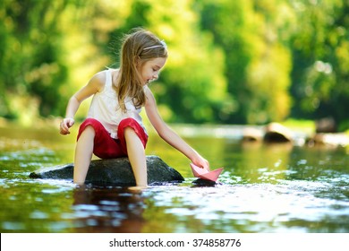 暖かく晴れた夏の日に川で紙の船で遊ぶかわいい女の子