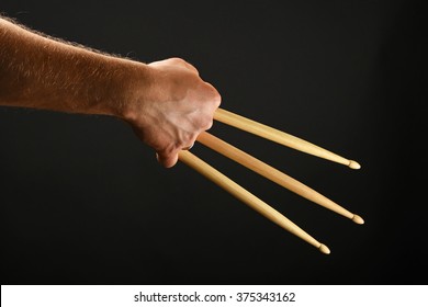 Gesto heroico de garras, mano de hombre sosteniendo tres baquetas de madera sobre fondo negro, vista posterior, horizontal