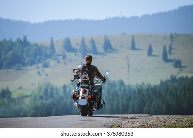 Junger Biker mit langen Haaren auf bergiger Straße. Mann fährt sein maßgeschneidertes Reisemotorrad auf der Autobahn. Blick von hinten.