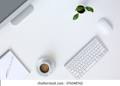 Vista superior del lugar de trabajo de tecnología moderna en el escritorio de oficina blanco con una gran computadora de escritorio Taza de café Teclado y mouse Flor verde Bloc de notas y bolígrafo