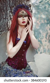 portrait of a beautiful red-haired girl in the image of the bird heat in the mask on the eyes, sitting on the branch of a tree, next to her large egg shells