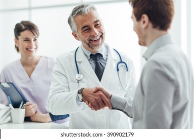 Smilende læge på klinikken giver et håndtryk til hans patient-, sundheds- og professionalismekoncept