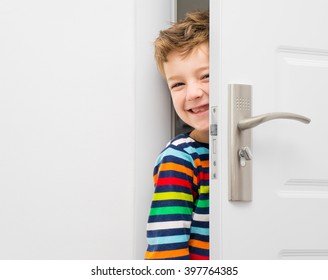 Gelukkige lachende jongen kijkt uit de deur op een kier. Het kind werd 's ochtends vroeg wakker en rende naar zijn ouders in de slaapkamer.