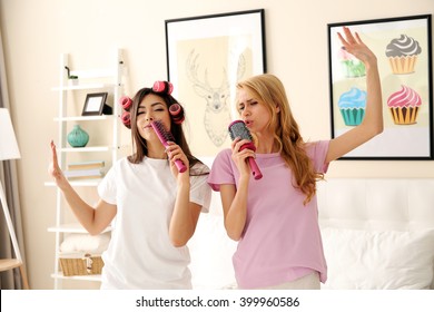 Twee meisjes zingen met kammen op een bed in de woonkamer