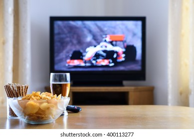 Televisyen, menonton TV (perlumbaan formula satu) dengan makanan ringan dan alkohol di atas meja - stok foto