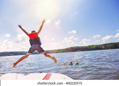 Niños saltando de un bote al lago. Concéntrese en las piernas y el bote de los niños, las lentes se encienden del sol.