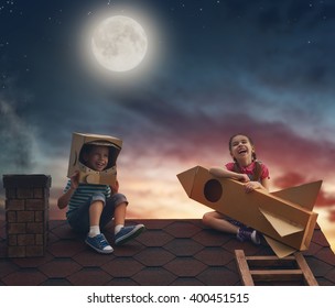 Children on the background of moon sky. Child boy in an astronaut costume and child girl with toy rocket standing on the roof of the house and looking at the sky and dreaming of becoming a spacemen.
