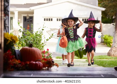 Three Children In Halloween Costumes Trick Or Treating