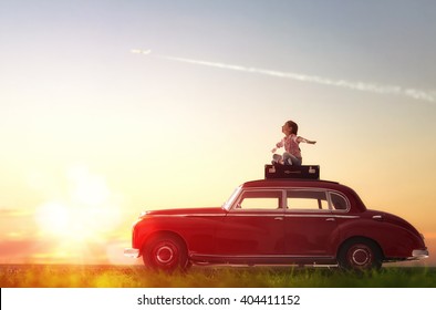 Toward adventure! Girl relaxing and enjoying road trip. Happy child girl sitting on roof of vintage car.