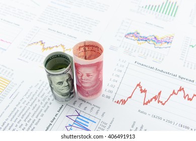 Rolled up scrolls of US dollar bill and Chinese Yuan with image / portrait of President Mao Zedong and Benjamin Franklin. Placing on financial reports with several charts i.e. colored linear graph.
