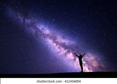 カラフルな紫色の天の川のある風景。丘の上に腕を上げて立っているスポーティーな女の子の星とシルエットを持つ夜空。美しい宇宙。宇宙背景