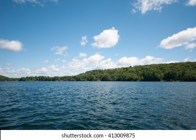 Blauw water aan het meer met eiland en bomen in de verte blauwe lucht met witte pluizige wolken