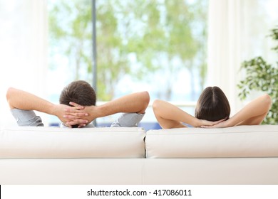 Rückansicht eines Paares, das sich zu Hause auf einem Sofa entspannt und durch das Fenster des Wohnzimmers vor einem grünen Hintergrund schaut