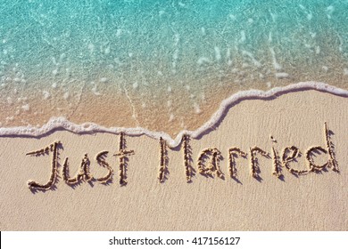 Recién casados ​​escritos en la arena de una playa tropical con una suave ola de océano azul en el fondo