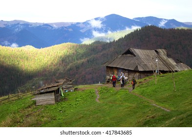 Wooden house in the mountains in spring, hut for the shepherd on the hill. A group of tourists near the house in the mountains.