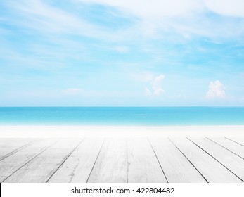 地平線の熱帯の砂浜に木製の床の前景を持つぼかしたクールな海の背景。太陽の光に触れるリゾートデッキで天国のような景色を眺めながら、屋外での休暇をリラックスし、夏の雲を空にサーフします。