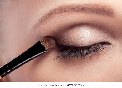 el artista de maquillaje trata el pincel de maquillaje para los ojos. maquillaje para una joven hermosa. sombra de ojos marrón. de cerca