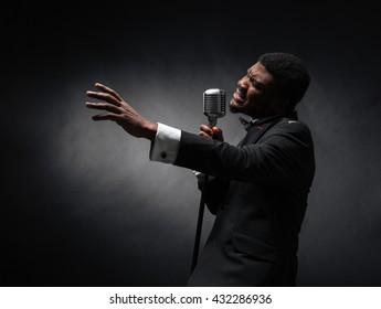 Afro american man singing into vintage microphone over dark background