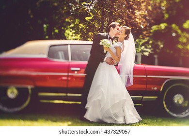 Pengantin lelaki memeluk pinggang pengantin perempuan mencium pipinya sebelum Dodge merah tua
