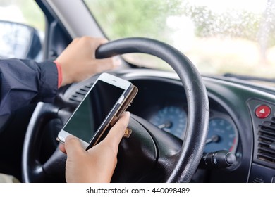 Closeup pada tangan orang yang memegang telepon dengan tampilan kosong, latar belakang roda mobil