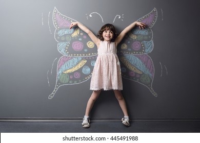 Đứa trẻ vui nhộn mỉm cười với đôi tay liều lĩnh với ước mơ trở thành con bướm. Rất lớn được miêu tả với côn trùng bằng phấn trên nền trung tính.