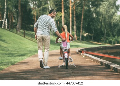 You can do it! Full length rear view of cheerful father teaching his daughter to ride a bicycle in park