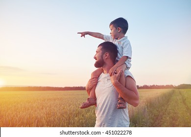 小さな男の子は父親の上に座って??s 肩と美しい日没時にフィールドで太陽を指しています。