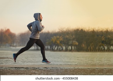 Junger athletischer Mann, der am kalten Herbstmorgen im Park läuft