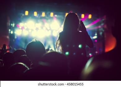 Silhouette eines Mädchens, das bei einem Live-Konzert nachts auf den Schultern sitzt.