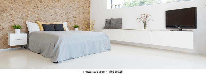 Spacious bedroom interior with the marital bed with cushions, commodes, TV and wooden wall on a bedhead