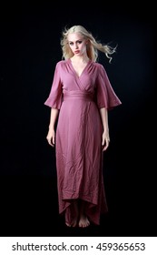 Beautiful blonde haired woman wearing a long flowing purple dress.   isolated on a black background.