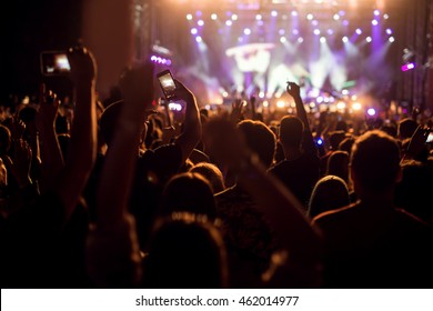 Menschen, die ein Konzert genießen, halten die Hände hoch und filmen mit ihren Smartphones.