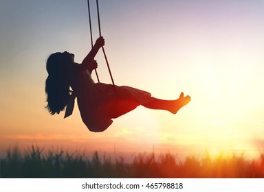 Happy laughing child girl on swing in sunset summer